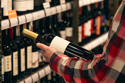 A male customer holding a bottle of red wine, close up.