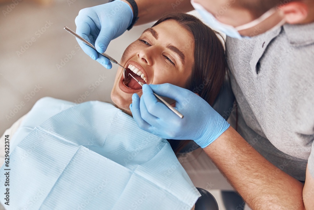 Confident mature doctor is checking teeth of young beautiful happy caucasian woman in modern clinic Confident mature doctor is checking teeth of young beautiful happy caucasian woman in modern clinic