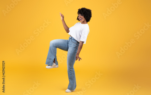 Cheerful young black woman in white t-shirt dancing alone, has fun isolated on orange background, studio, full length photo