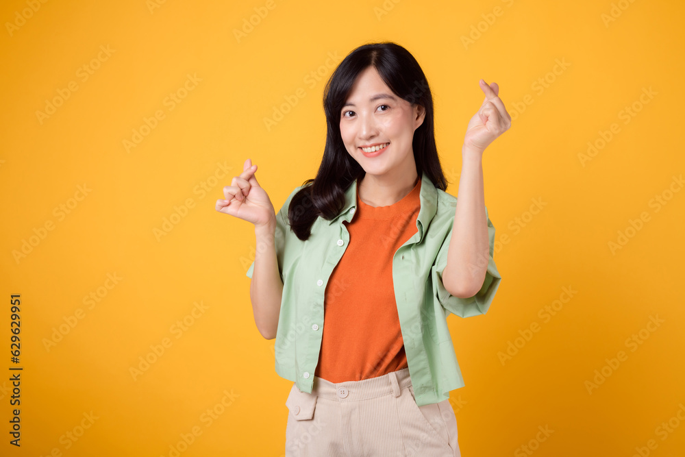warmth of affection and happiness with young Asian woman 30s, dressed in an orange shirt and green jumper. Her mini heart gesture and gentle smile express a profound message through body language. warmth of affection and happiness with young Asian woman 30s, dressed in an orange shirt and green jumper. Her mini heart gesture and gentle smile express a profound message through body language.