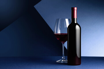Bottle and glass of red wine on a blue background.