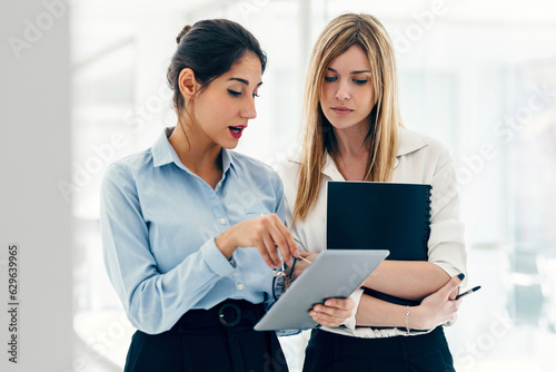 Two elegant attractive businesswomen working with digital tablet while talking in a modern startup