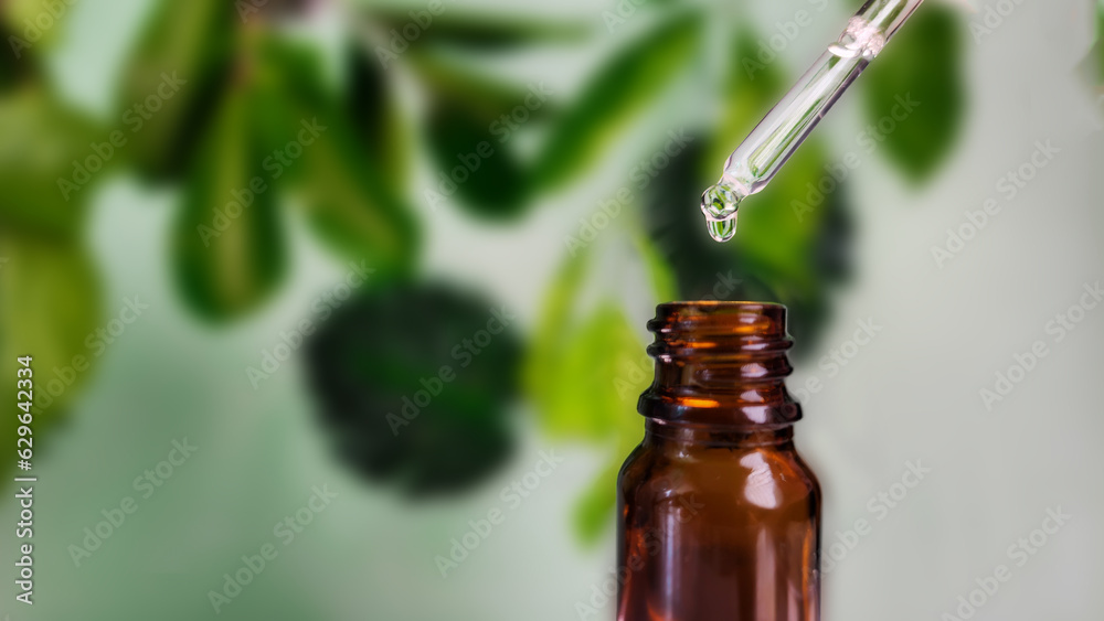 Dripped of natural oil or serum over glass bottle, spill serum natural, tree and leaves background with copy space