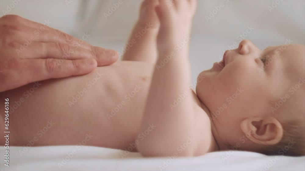 Close-up of father hands massaging little baby. Newborn Baby skin care concept. Prevention of colic. Male hands doing massage to newborn. Nice caucasian infant baby lying on cozy bed. Slow motion Close-up of father hands massaging little baby. Newborn Baby skin care concept. Prevention of colic. Male hands doing massage to newborn. Nice caucasian infant baby lying on cozy bed. Slow motion