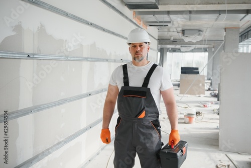 A man with a beard in a helmet and work clothes. Portrait of a worker in workwear with copy space.