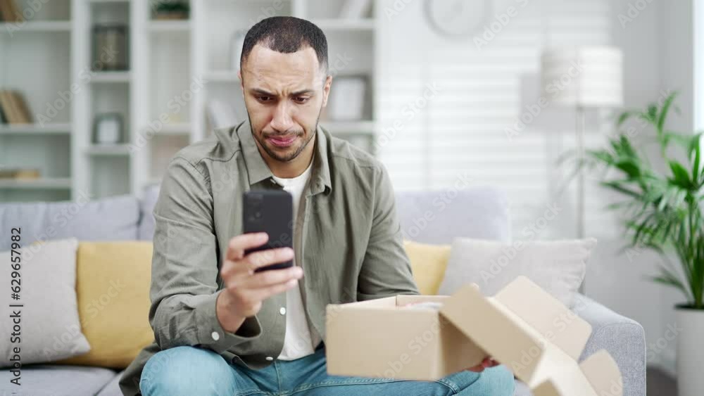 Angry dissatisfied client arabian man receive broken carton bad parcel delivery box having negative shopping experience write complaints in mobile phone give bad negative feedback at home indoor Angry dissatisfied client arabian man receive broken carton bad parcel delivery box having negative shopping experience write complaints in mobile phone give bad negative feedback at home indoor
