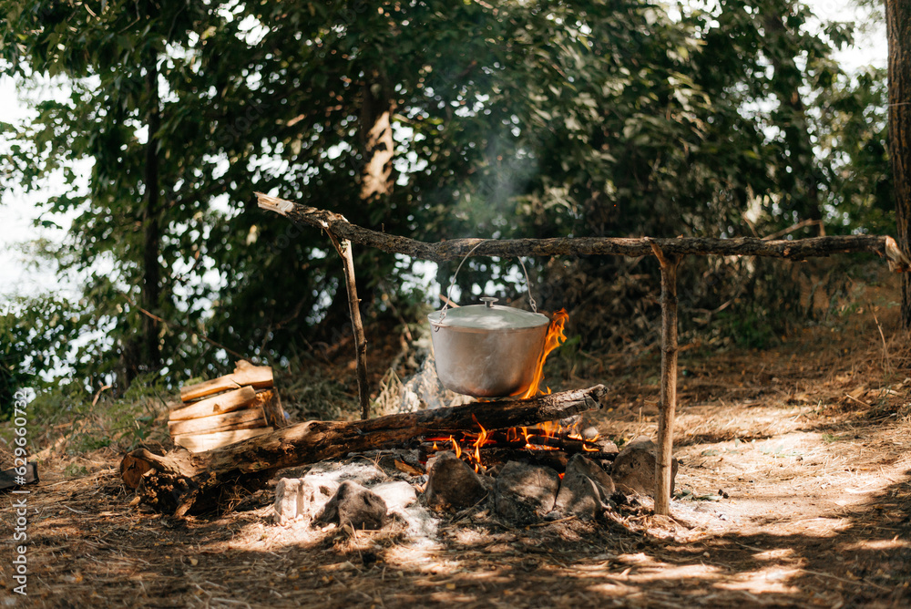 Travel a kettle over a fire burning on the river and sunset backgroun. Cooking over a campfire Travel a kettle over a fire burning on the river and sunset backgroun. Cooking over a campfire