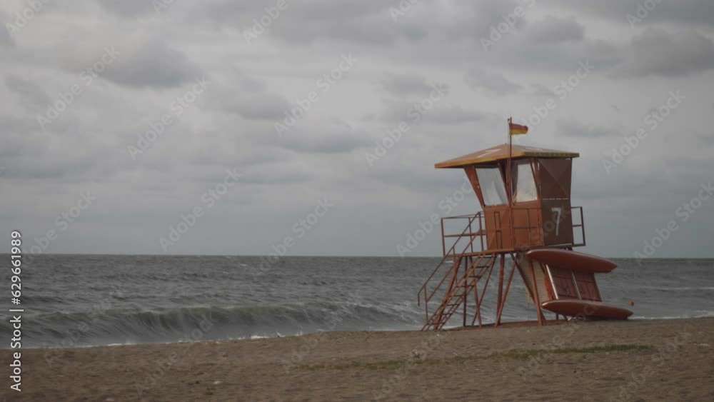 Lifeguard observation desk with red flag in front of wild sea waves on bad cold windy cloudy weather, no swimming allowed, nobody on the beach Lifeguard observation desk with red flag in front of wild sea waves on bad cold windy cloudy weather, no swimming allowed, nobody on the beach