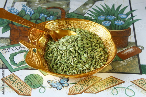 heap of dried organic green fennel seeds also known in india as valiyari mouth freshener or Saunf herb isolated in golden dish with spoon, top view