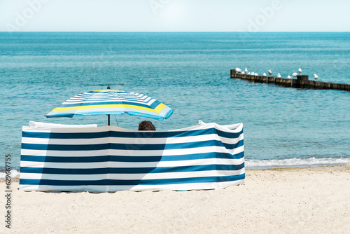 Fototapeta Naklejka Na Ścianę i Meble -  A parasol and a cheerful blue and white striped windbreak on the summer beach of the Baltic Sea in Western Pomerania, Kühlungsborn.