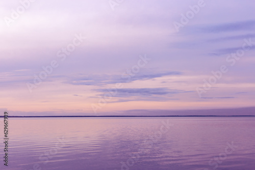 Minimal Colorful sky background on sunset, purple pastel color clouds and surface water on lake Ik. Nature abstract composition with reflections on water, natural blue pink shades of skyline