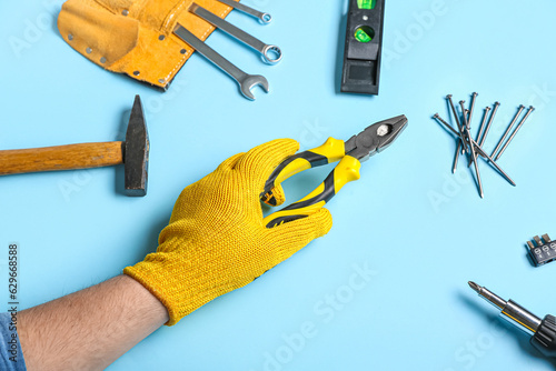 Male hand in gloves holding pliers near different instruments on blue background photo
