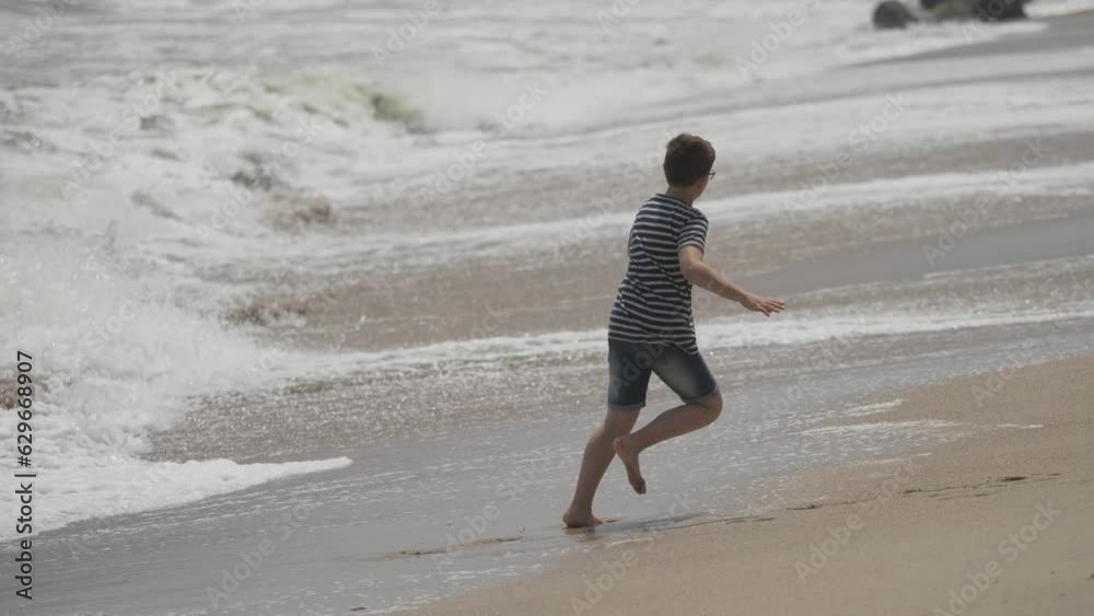 Big boy playing barefoot with the sea waves on the beach Big boy playing barefoot with the sea waves on the beach