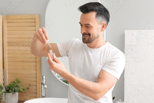 Handsome man with serum for hair growth in bathroom