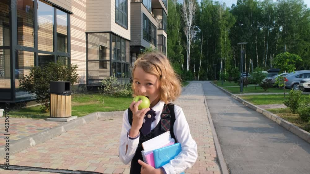 Cheerful little girl eating apple while holding notebooks in hands, going to classes in the morning. Back to school Cheerful little girl eating apple while holding notebooks in hands, going to classes in the morning. Back to school