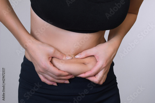 close up photo of young woman hand holding excessive belly fat on gray background. Health concept