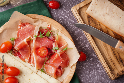 Plate with slices of tasty jamon and cheese on grunge background, closeup