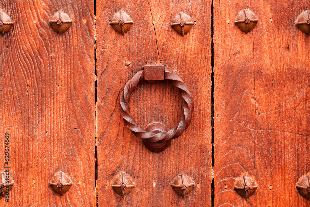 An ancient ornate iron knocker on an old wooden entrance door An ancient ornate iron knocker on an old wooden entrance door