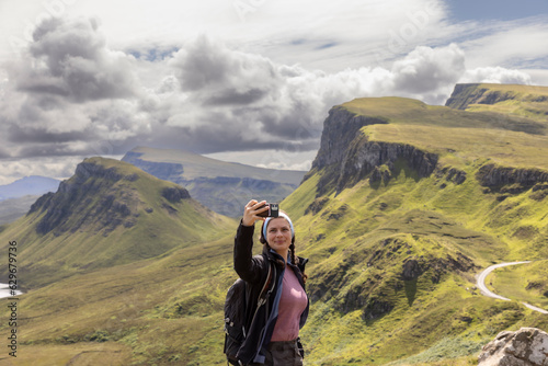 Young woman making selfie with smartphone on mountain range Quiraing. It is a geological formation on the Scottish Isle of Skye and a hiker's paradise