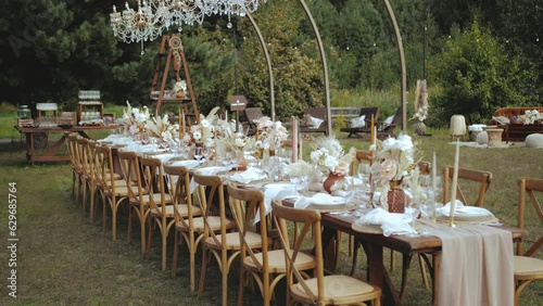 Wedding table outdoor decorated with candles and dried pastel flowers for boho style wedding dinner, plates and wine glasses, wind shakes tablecloth, napkings and floristic composition. photo