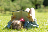 A girl is lying and reading her favorite book on a green meadow covered with yellow flowers in a nice sunny summer, spring day. Concept of recreation, education and study, curiosity, leisure time