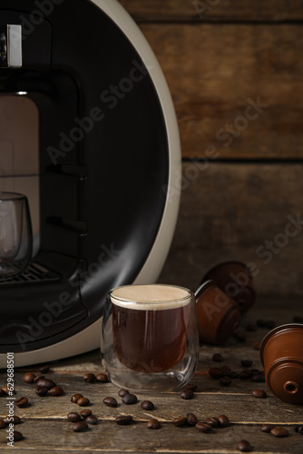 Foto Glass of delicious espresso, capsule coffee maker, pods and beans on wooden tabl