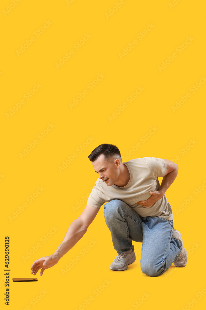 Young man with mobile phone having heart attack on yellow background Young man with mobile phone having heart attack on yellow background