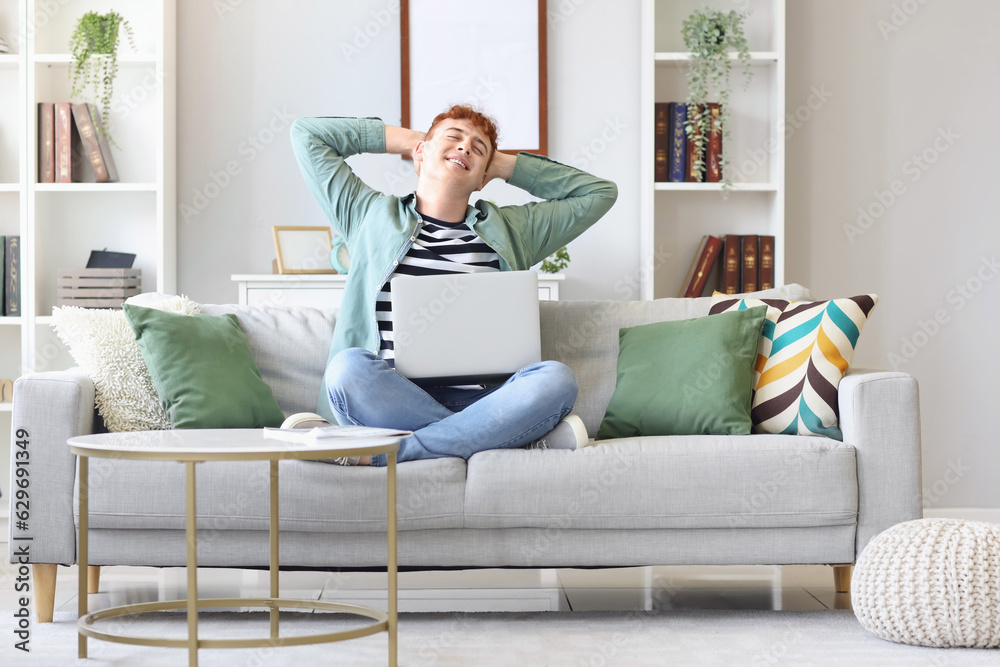 Young redhead man with laptop stretching on sofa at home Young redhead man with laptop stretching on sofa at home