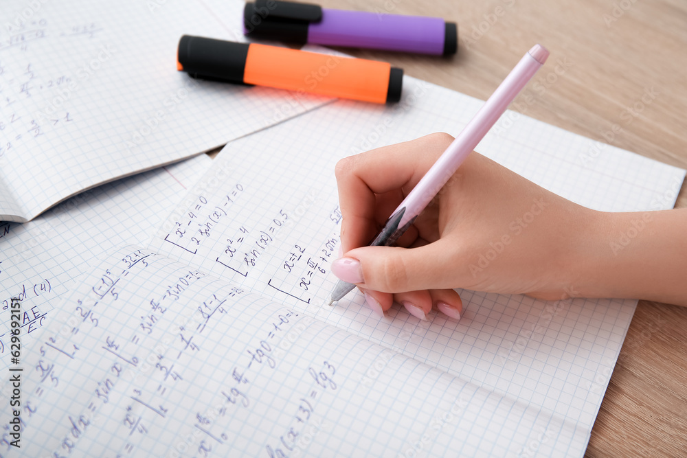Woman writing math formulas in copybook on wooden table Woman writing math formulas in copybook on wooden table
