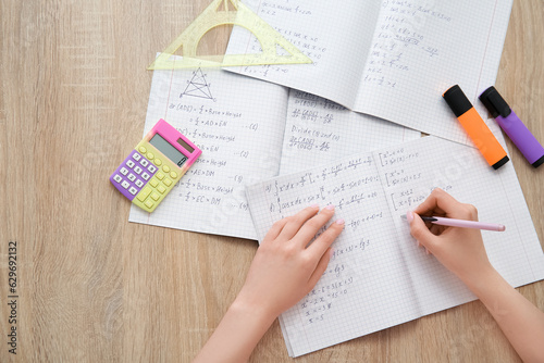 Woman writing math formulas in copybook on wooden table photo