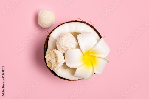 Coconut with white chocolate candies and plumeria flower on pink background