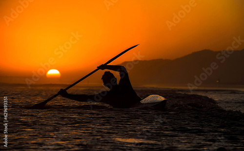 Silhouette of a man doing kayaking in the beach at the sunset 
