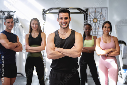 group of fitness and multi-ethnic people posing for the camera with their arms crossed at the gym