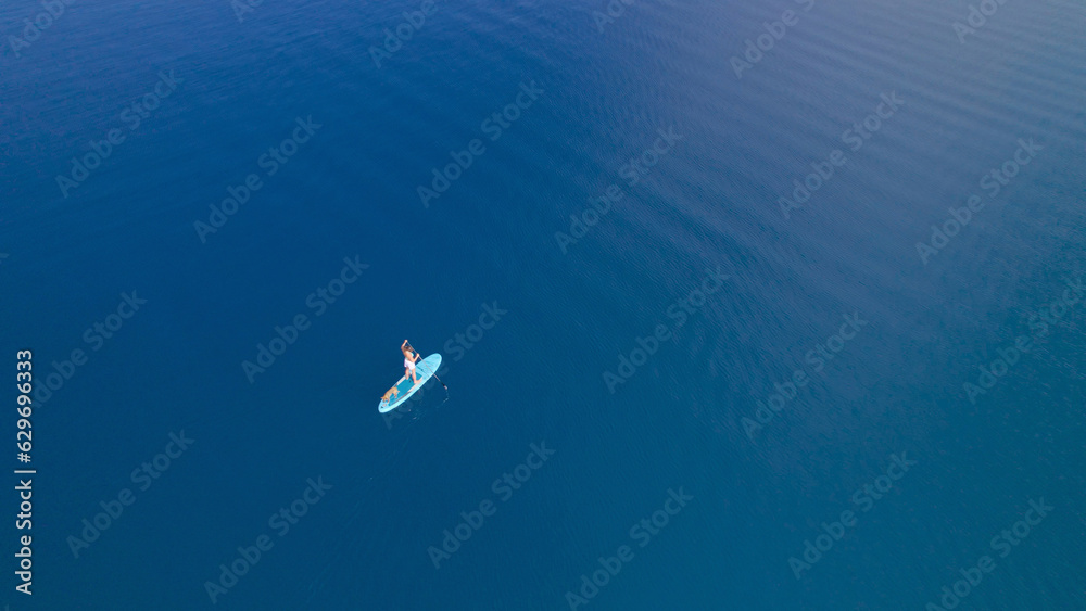 AERIAL: Intense deep blue sea water and pretty lady paddling on SUP with her dog