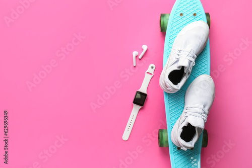 Smartwatch, earphones, sneakers and skateboard on pink background