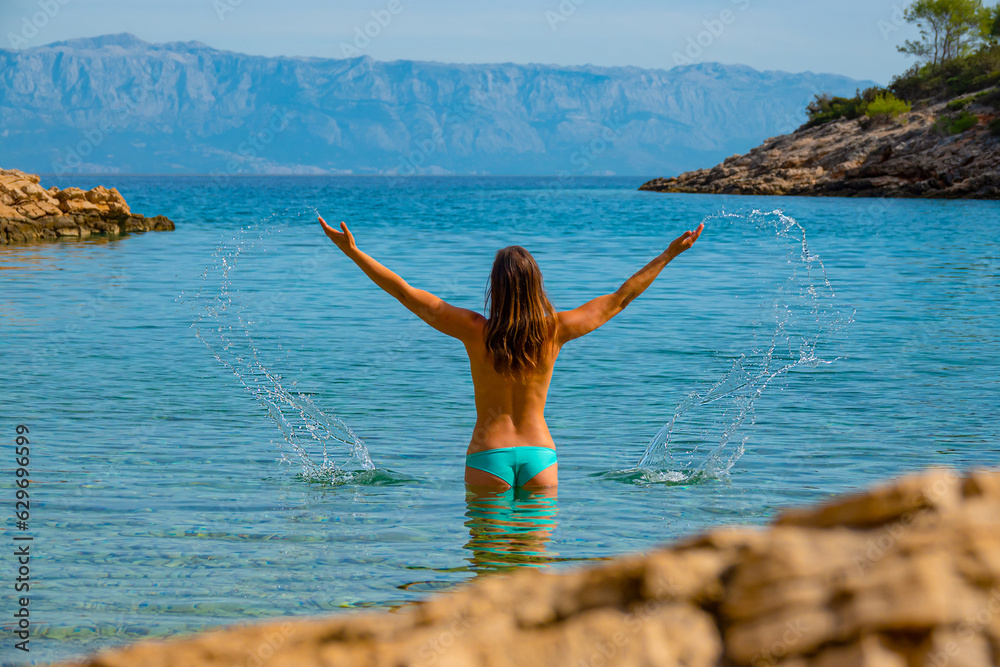 Carefree young lady splashes water while going for a topless swim in blue sea Carefree young lady splashes water while going for a topless swim in blue sea