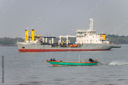 A fishing boat sails in the Chao Phraya River, a dredger boat on the background, Thailand photo