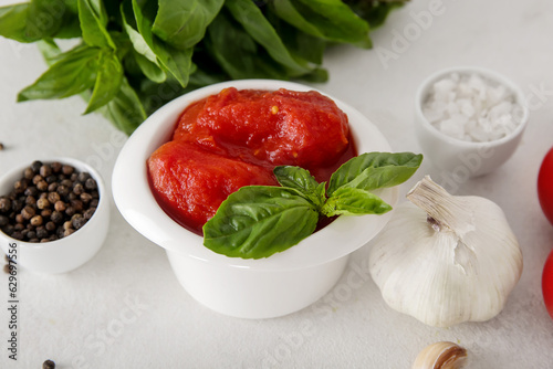 Bowl of canned tomatoes and spices on light background