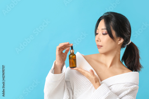 Beautiful young Asian woman with essential oil on blue background