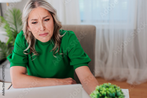 White blonde woman sitting at desk with laptop in home office space wearing a green shirt