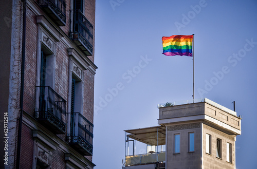 Rainbow Flag of the Gay LGBTQ Community Waving on Top of a Building Over Blue Sky photo