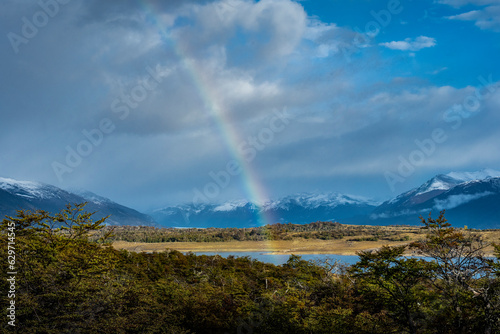 Rainbow over a lake with trees in front and snow-capped mountains behind in Los Glaciares National Park, Santa Cruz, Argentina.