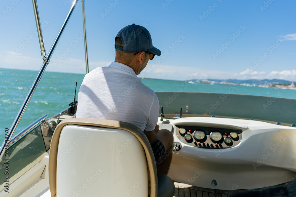 Naklejka premium Bach view of middle-aged man driving luxury motor yacht. Captain at the helm of motor boat.