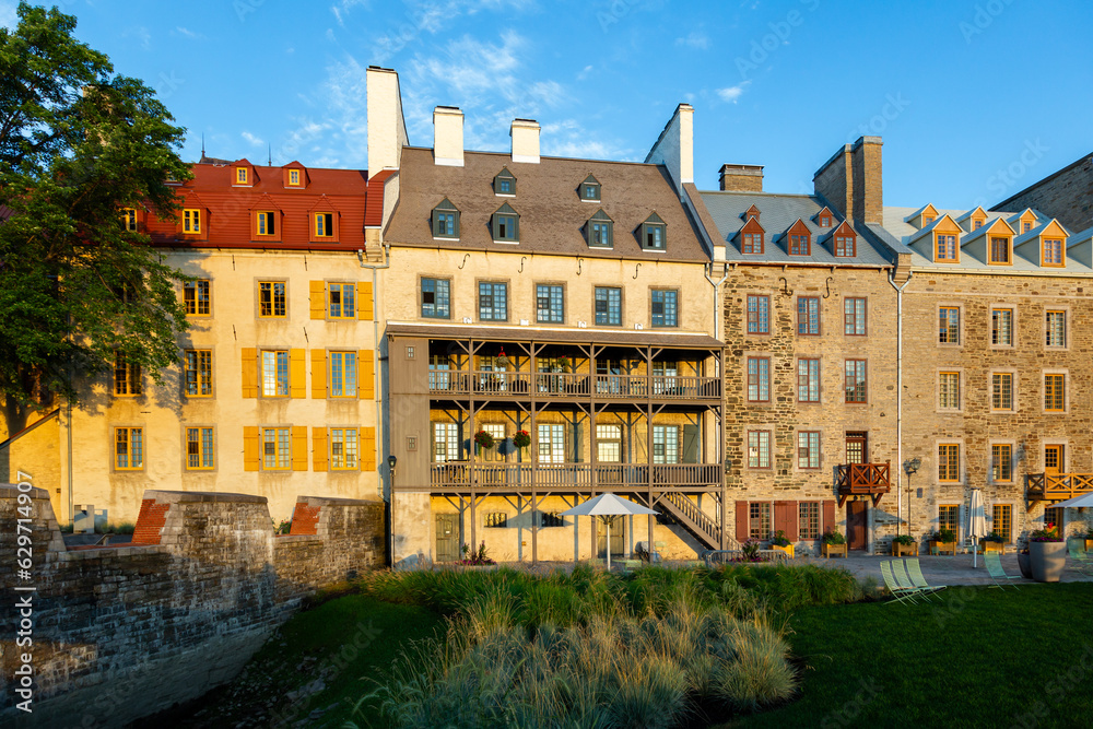 Historic buildings on Place de Paris in the Petit-Champlain sector with metal chairs on lawn in the foreground seen during a summer golden hour morning, Quebec City, Quebec, Canada