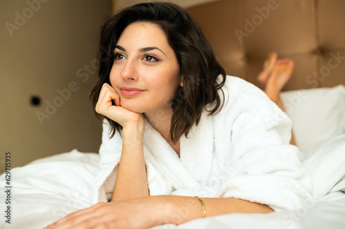 Young woman lying in bed at home in a smiling pensive expression