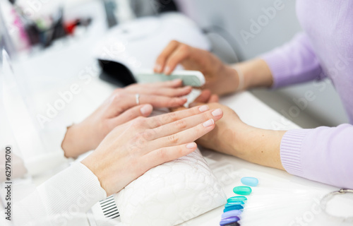 Young woman hands in a nail salon, which the manicure master files the nails with a nail file, giving them shape