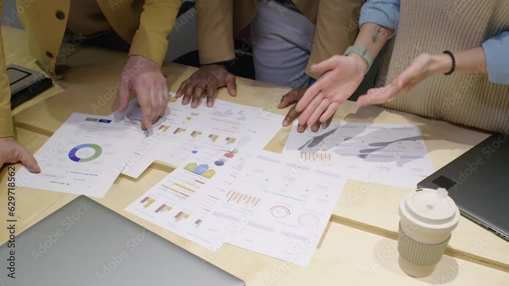 High angle close up of project documents with diagrams and graphs lying on table and unrecognizable managers looking at them and discussing High angle close up of project documents with diagrams and graphs lying on table and unrecognizable managers looking at them and discussing
