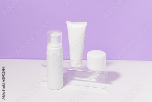 Horizontal image of a white mockup set of a tube and a jar of cream and foam on a purple background. The concept of daily care cosmetics for the face and body, moisturizing and beauty treatments