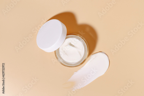 Foto Glass jar of facial moisturizer and smear on beige isolated background