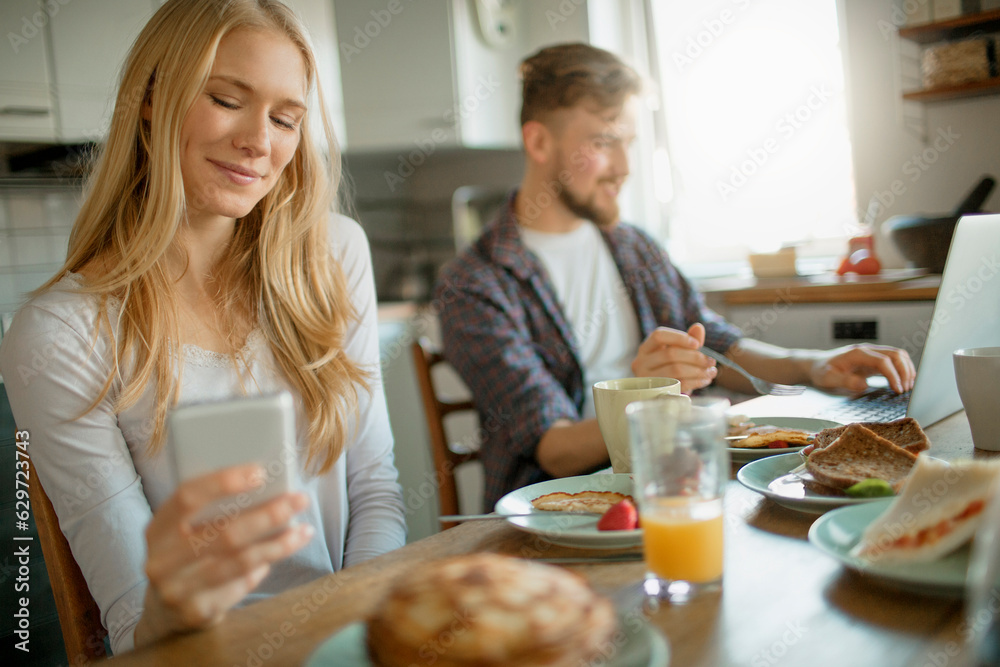 Young couple using a smart phone while having breakfast in the kitchen in the morning Young couple using a smart phone while having breakfast in the kitchen in the morning